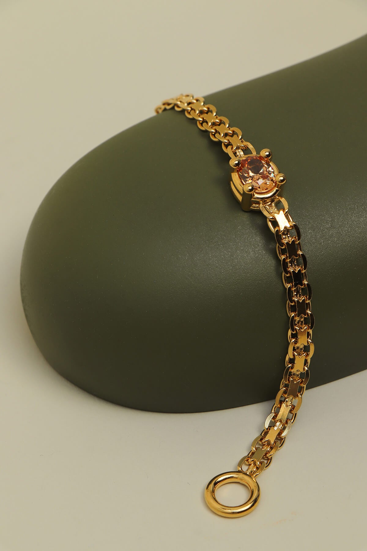 Gold-plated Drip T-lock bracelet with cubic zirconia featuring an oval orange cubic zirconia in an oversized four-prong setting resting on a curved green display form.