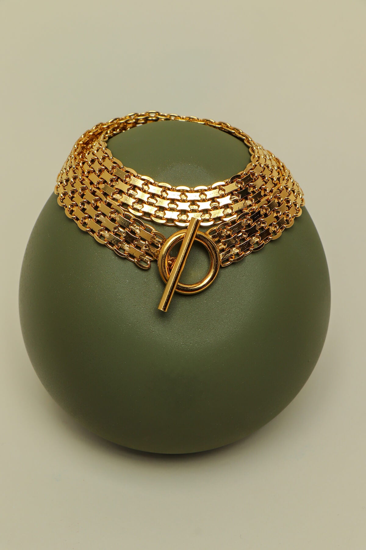 Drip T-lock bracelet featuring a bold T-bar clasp draped over a sculptural green display form.