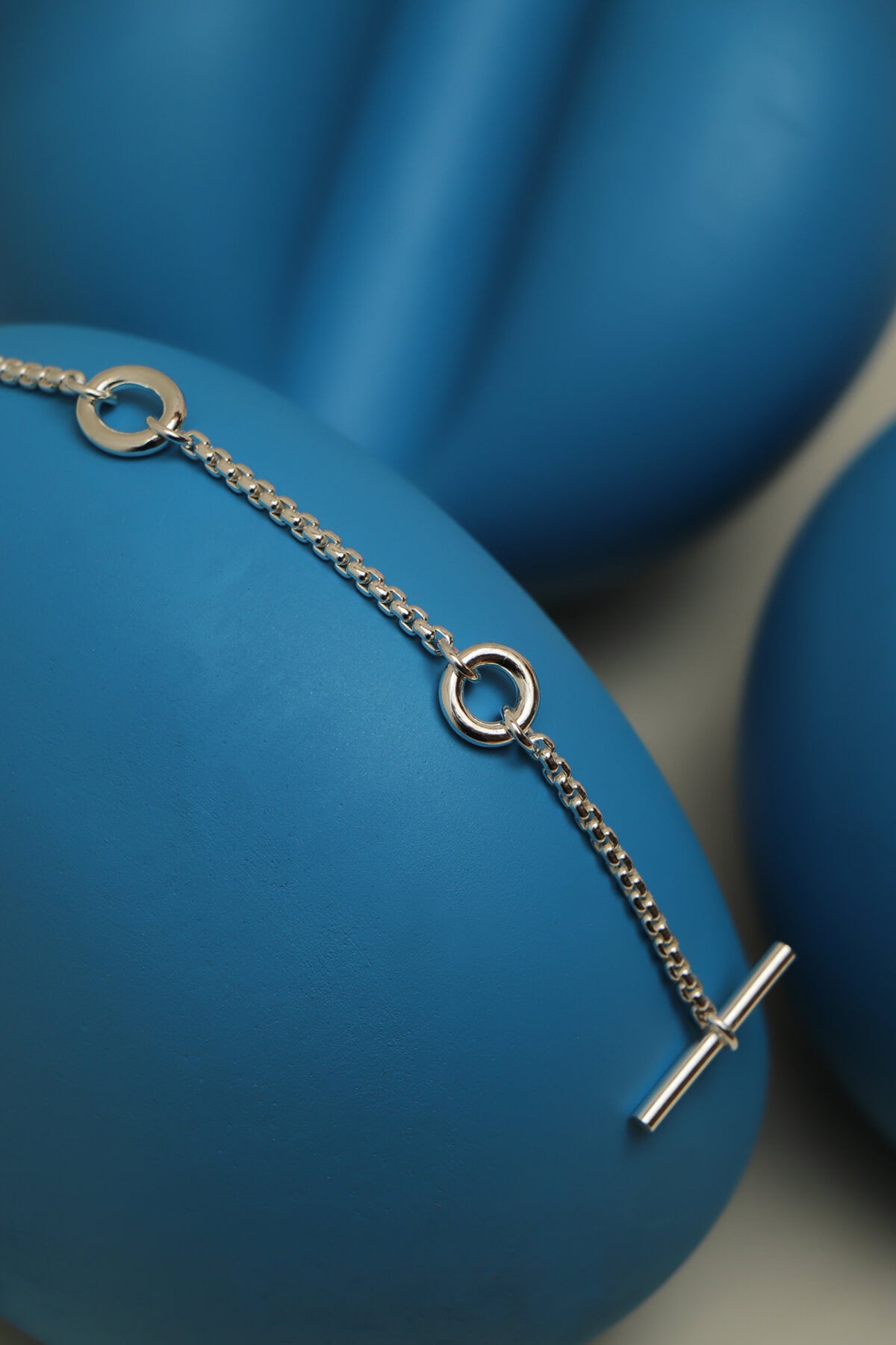 Splash bracelet featuring a fine chain with a T-bar clasp draped over sculptural blue display forms.