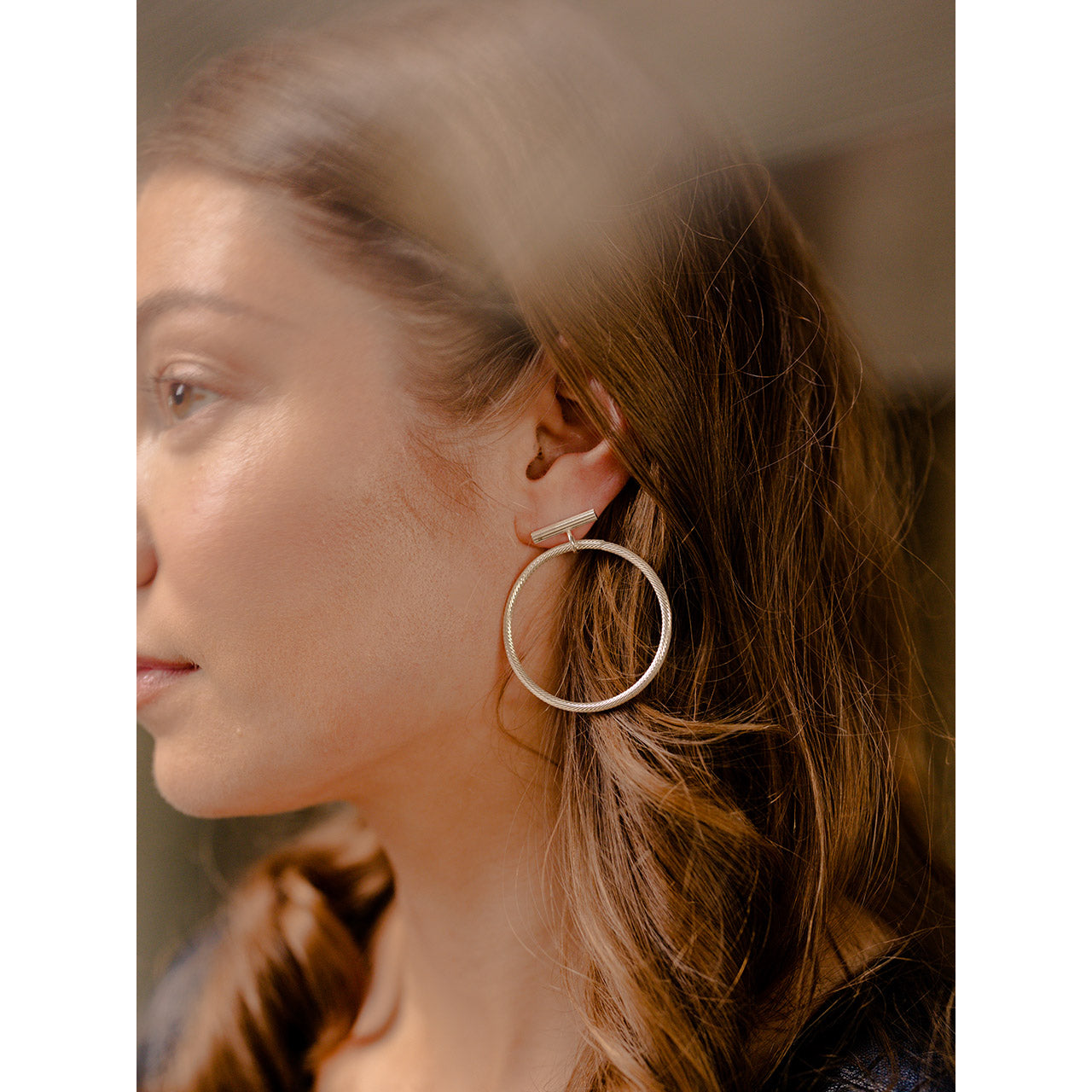 These earrings boast a round horizontal bar adorned with an intricately engraved pattern, and a loop at its center.
