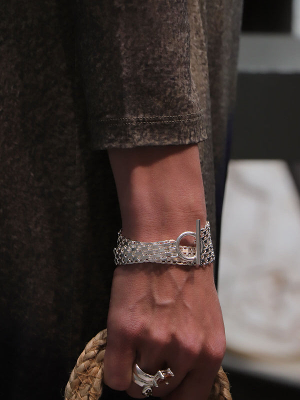 Drip T-lock bracelet worn with the Drip Drop ring in a close-up of the hand holding a woven handbag.