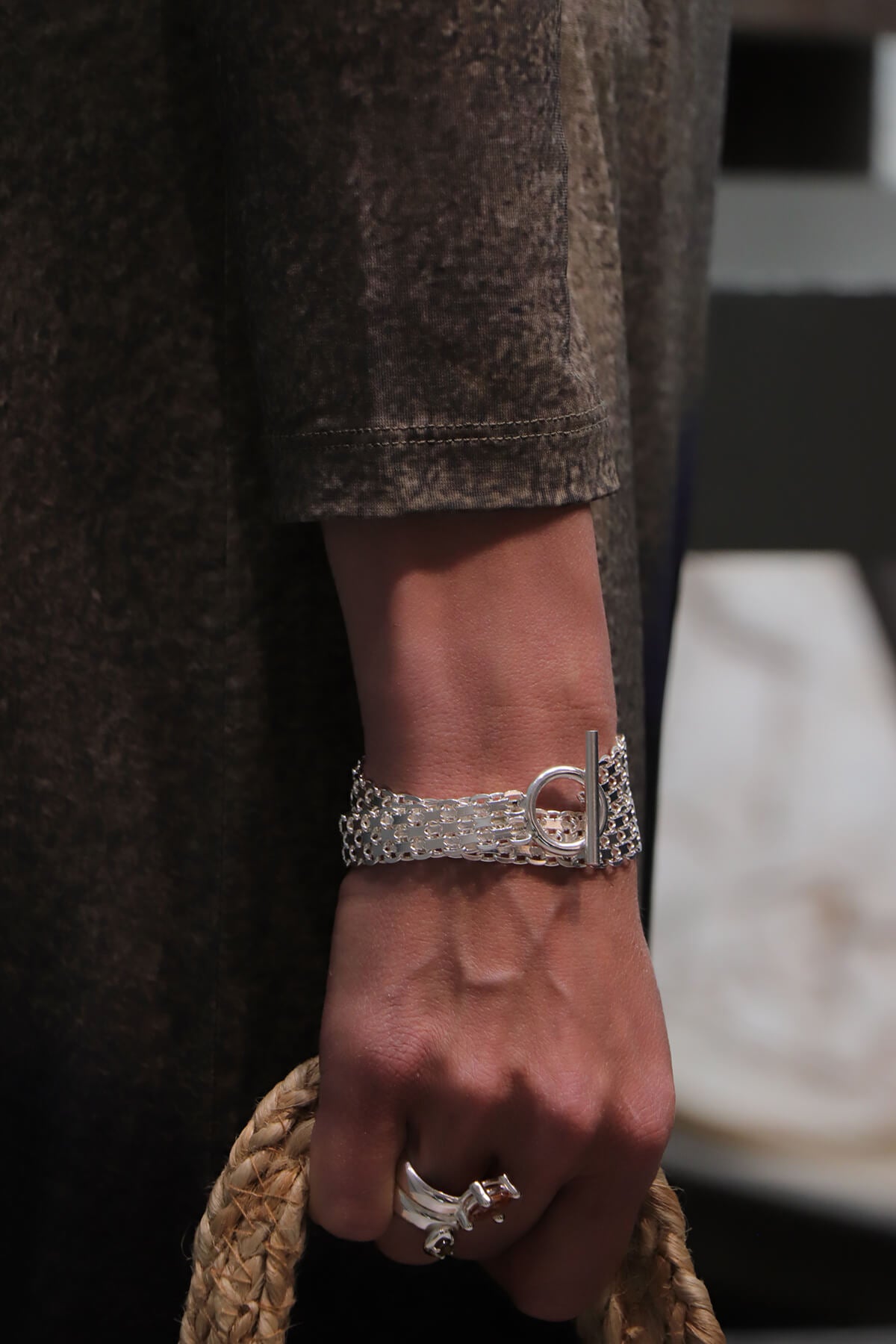 Drip T-lock bracelet worn with the Drip Drop ring in a close-up of the hand holding a woven handbag.