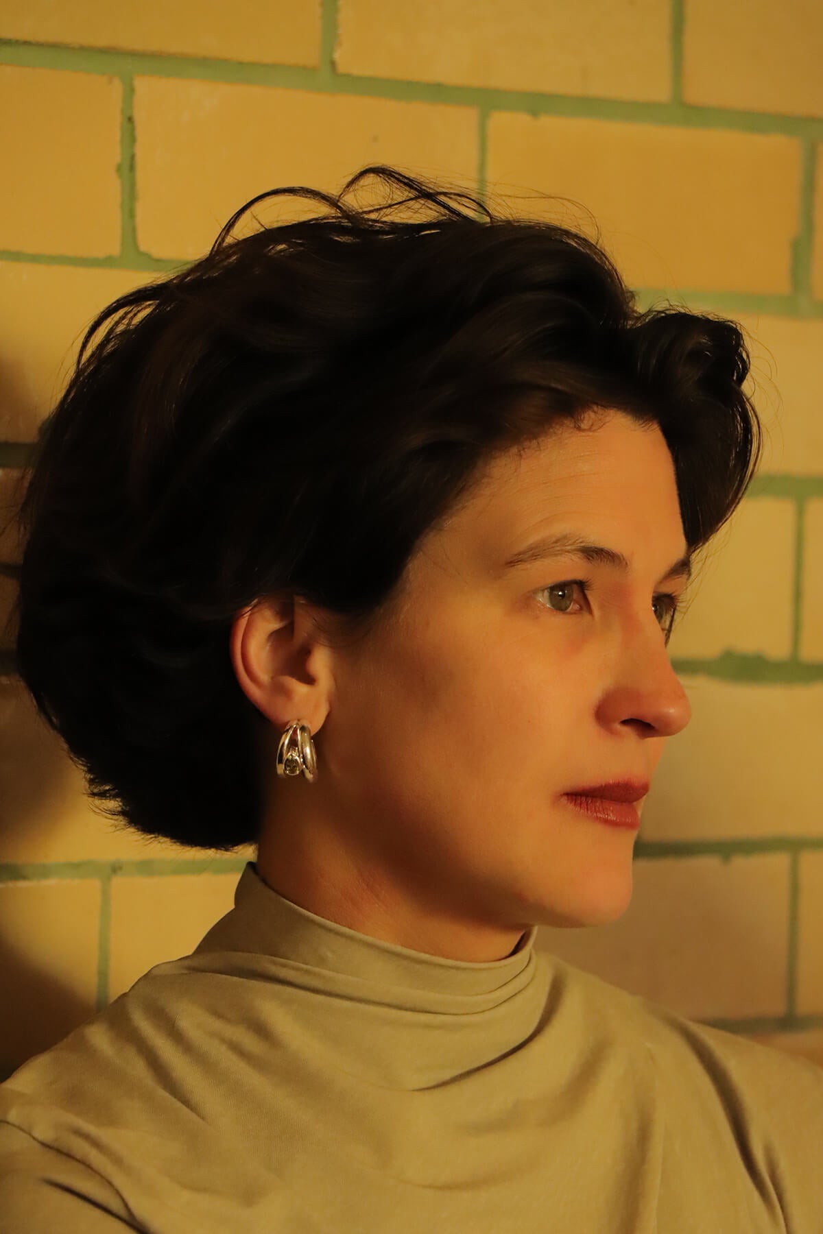 Hannah wearing Drop hoops with green pear-cut cubic zirkonia in a side profile portrait at La Piscine Musée Roubaix.