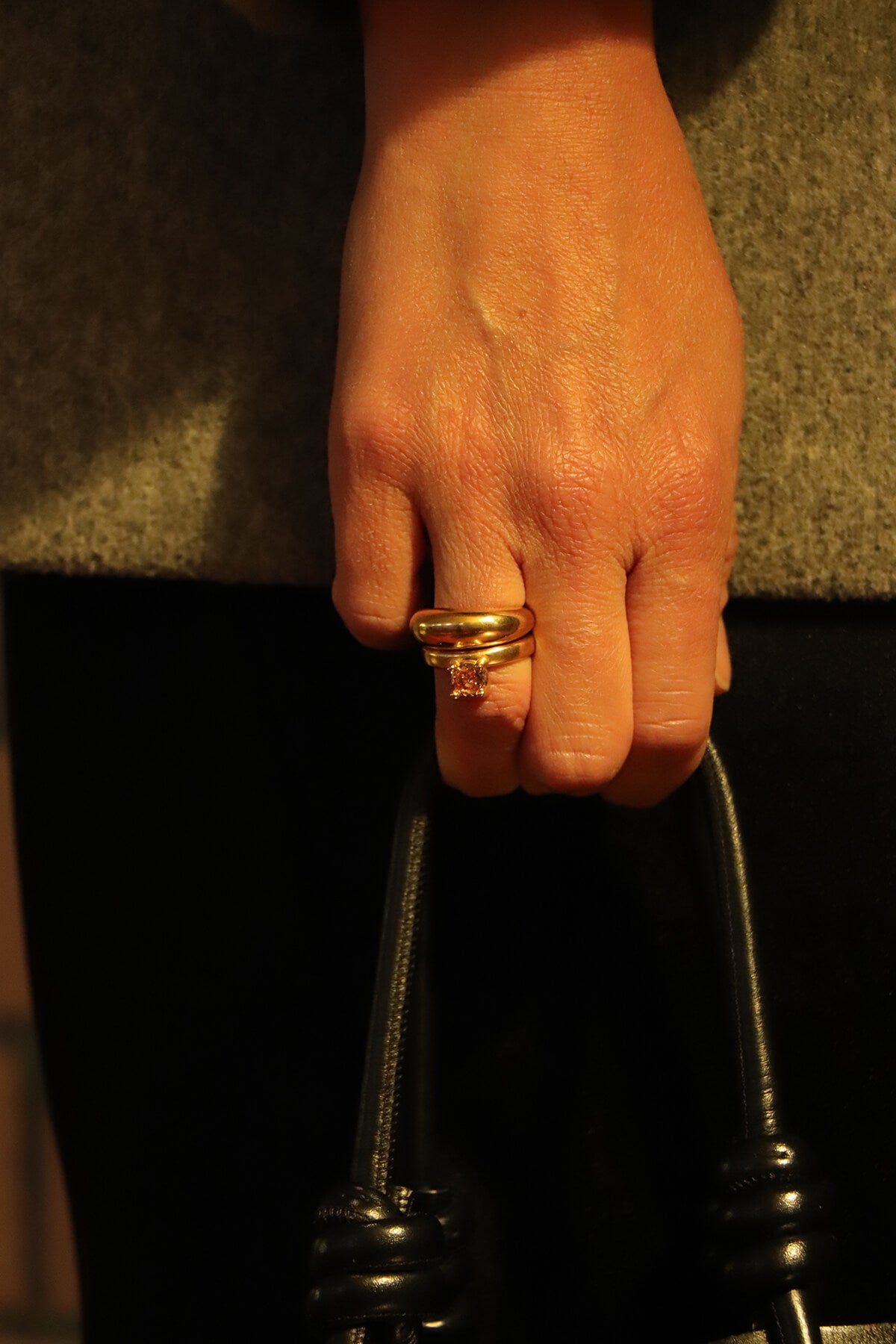 Drip ring with round cubic zirconia worn on the finger while holding a black handbag at La Piscine Musée Roubaix.