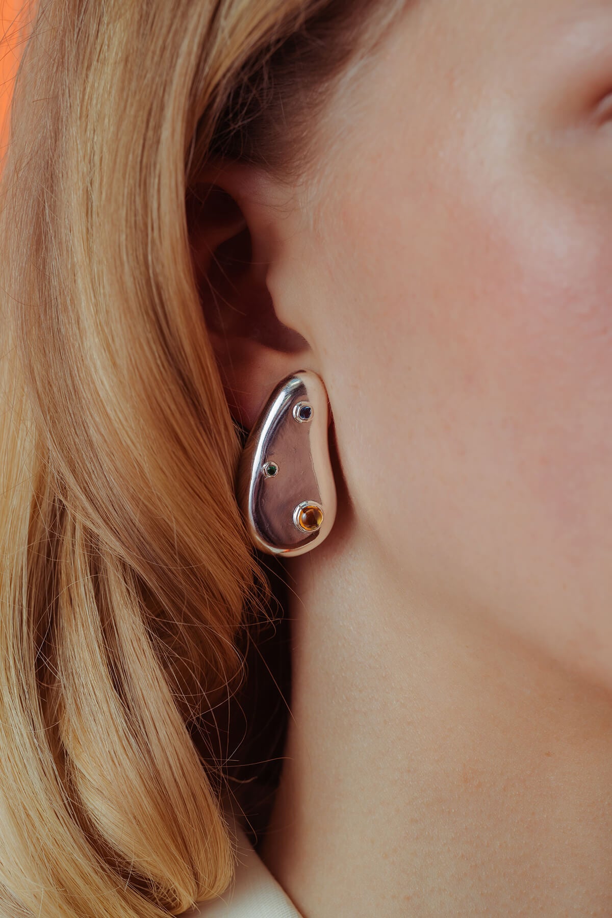 Spill earrings with cubic zirconia in silver featuring blue, green and orange stones on a sculptural droplet shape.