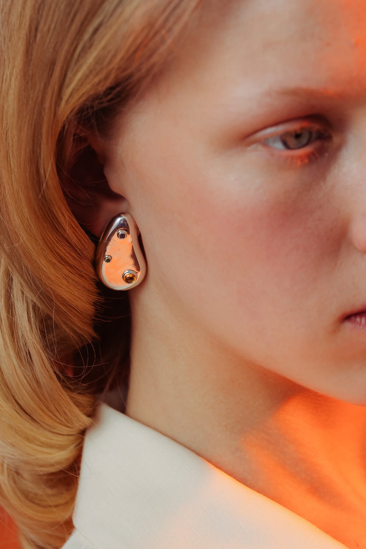 Spill earrings with cubic zirconia in silver showing a polished droplet shape with blue, green and orange stones.