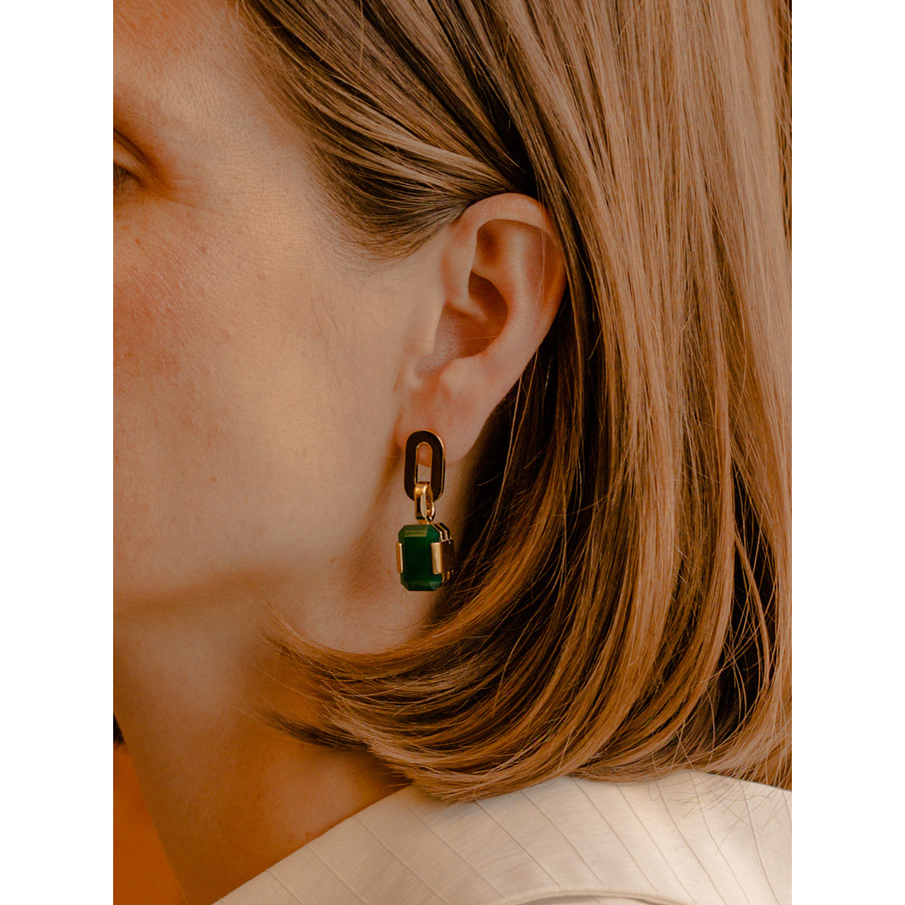 An oval-shaped element gracefully adorns the earlobe, accompanied by a large resplendent green agate pendant.
