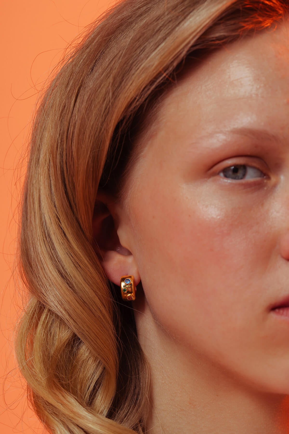 Spill hoops with cubic zirconia in a gold-plated finish featuring blue, green and orange stones in a rounded hoop.