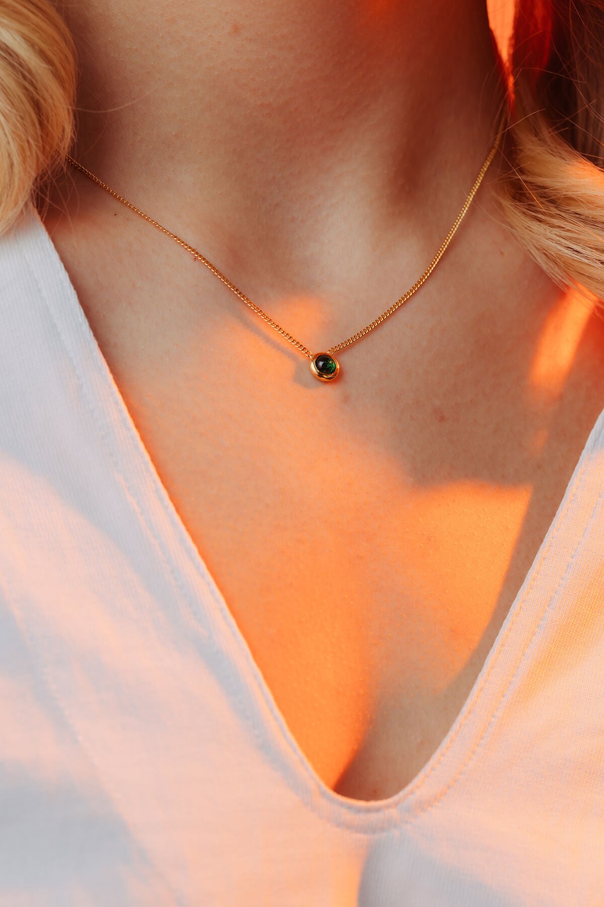 Bubble necklace with cubic zirconia featuring a green cabochon pendant on a fine gold-plated chain worn at the neckline.