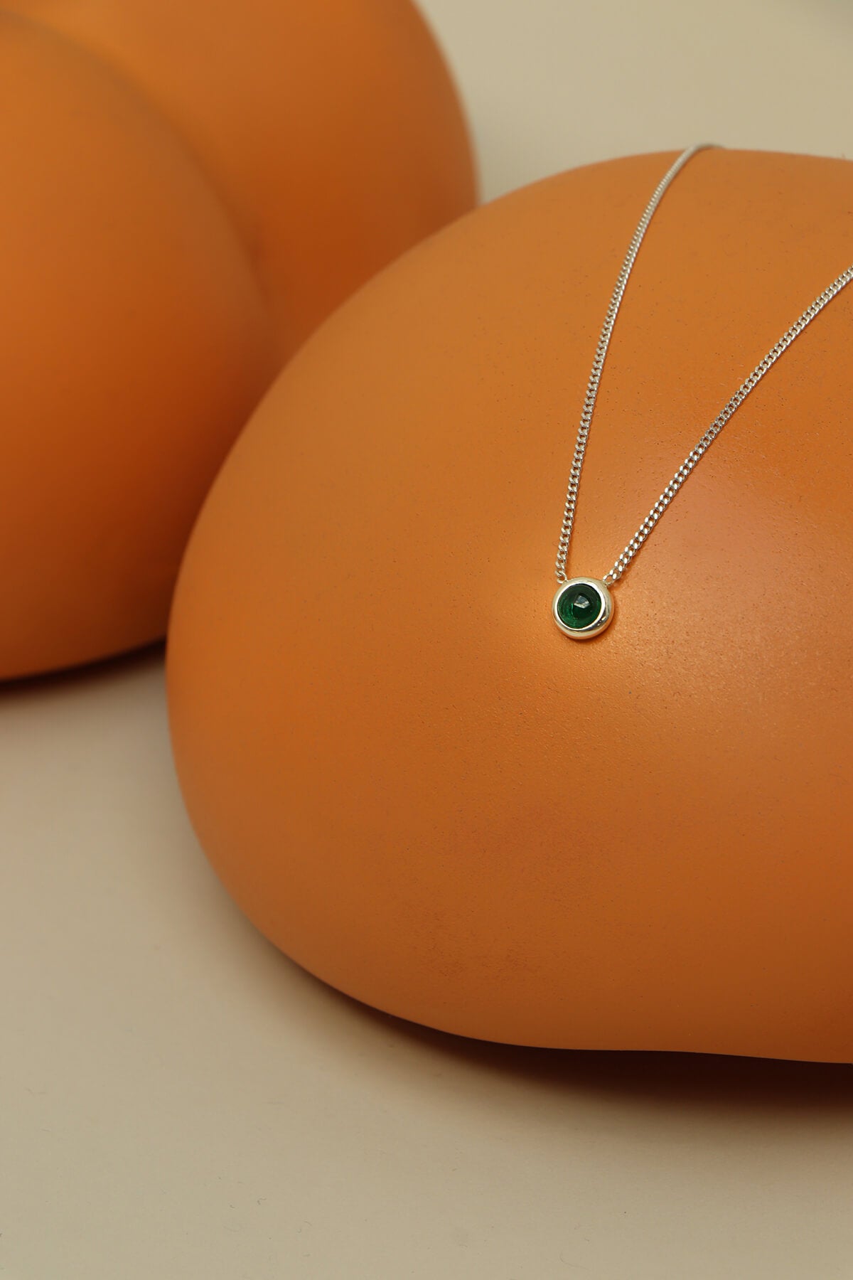 Bubble necklace with cubic zirconia featuring a green bezel-set stone on a fine chain displayed across rounded orange forms.