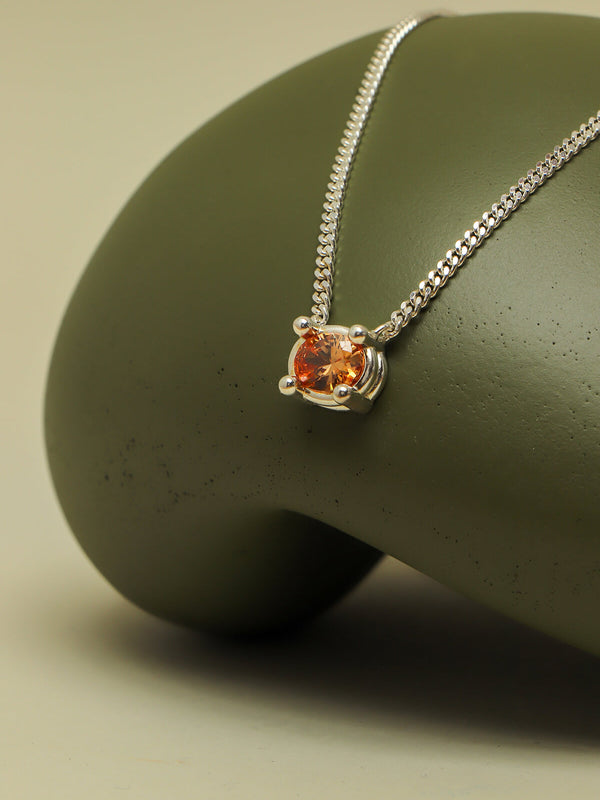 Drip necklace with cubic zirconia showcasing an orange oval stone in an oversized four-prong setting on a sculptural green form.