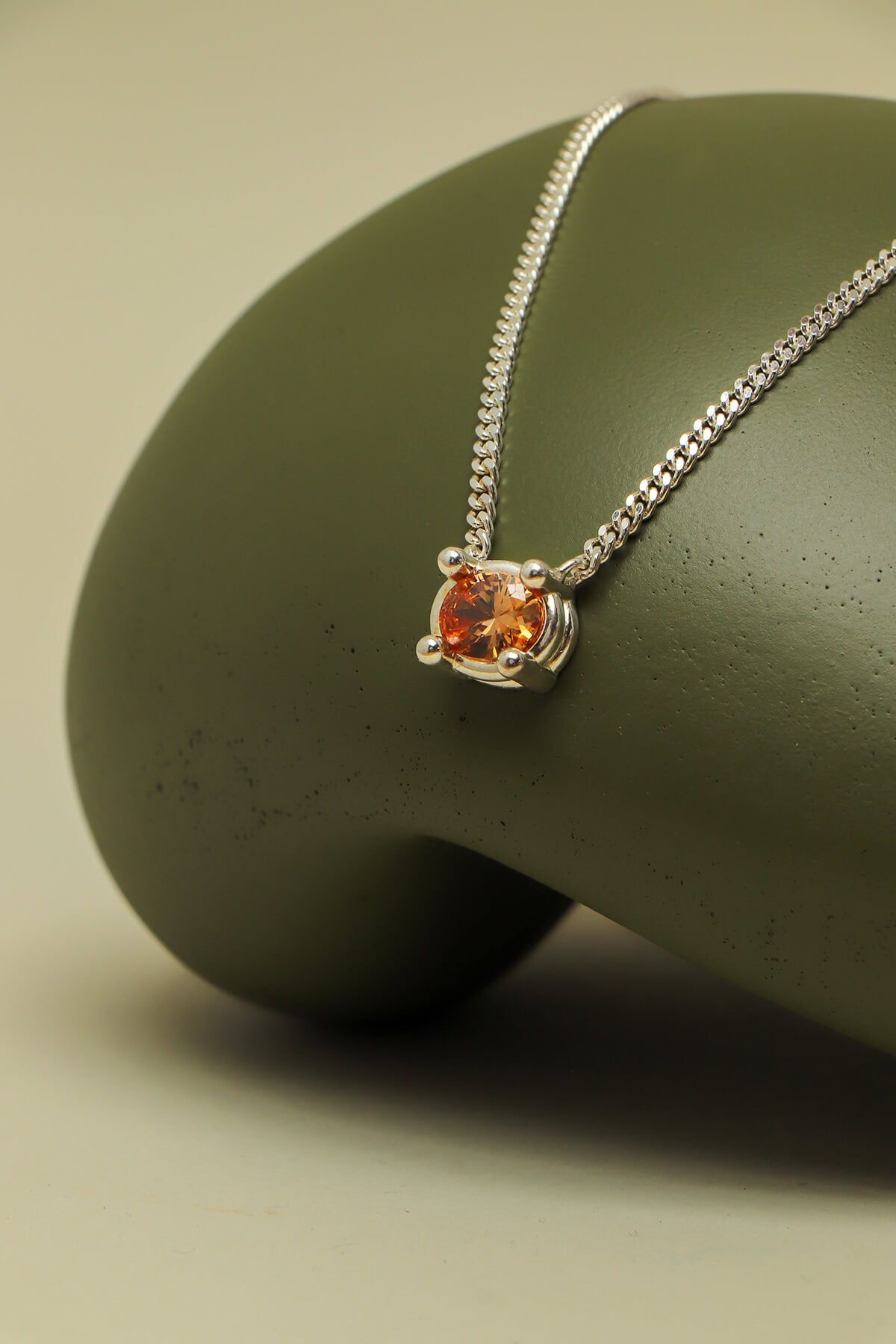 Drip necklace with cubic zirconia showcasing an orange oval stone in an oversized four-prong setting on a sculptural green form.