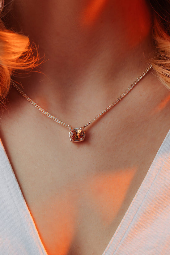 Drip necklace with cubic zirconia with an oval orange cubic zirconia in an oversized four-prong setting on a silver chain.
