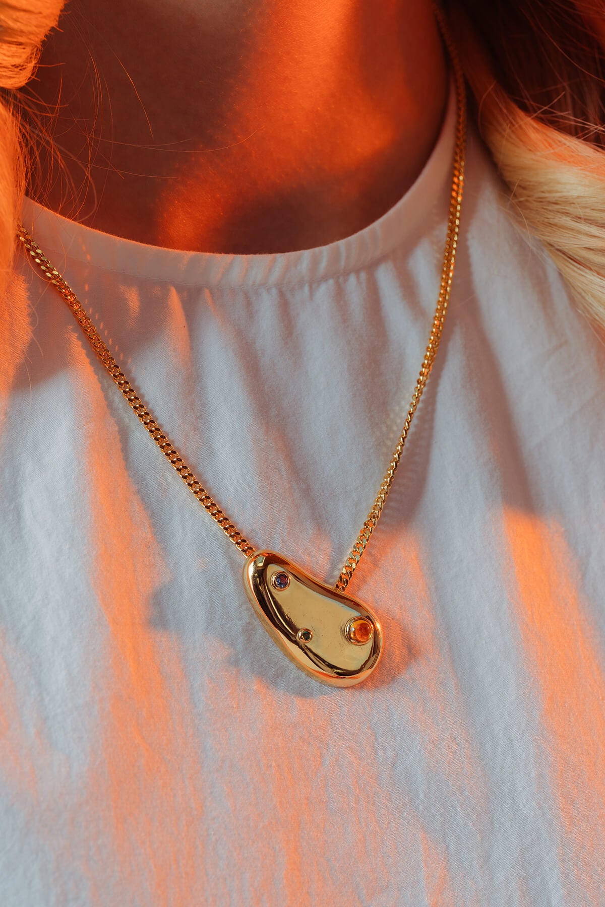 Spill necklace with cubic zirconia worn in warm light with an organic pendant featuring blue, green and orange stones.