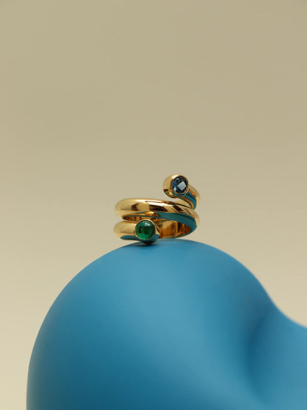 Bubble twist ring with cubic zirconia featuring blue and green bezel-set stones on a smooth blue sculptural form.