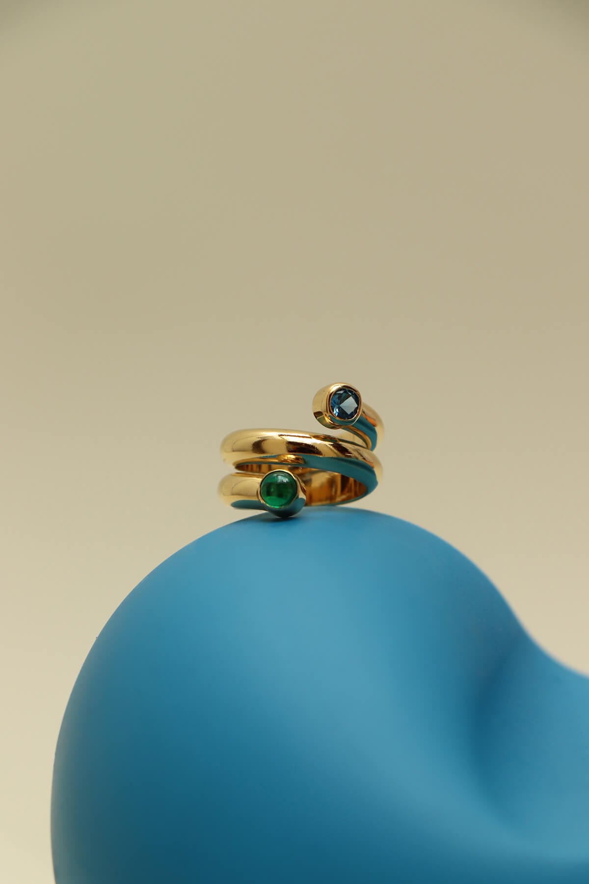 Bubble twist ring with cubic zirconia featuring blue and green bezel-set stones on a smooth blue sculptural form.