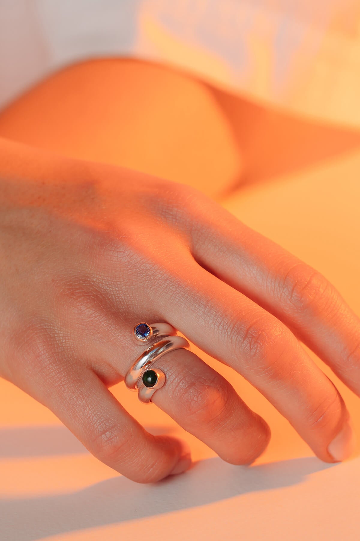 Bubble twist ring with cubic zirconia featuring a sculptural twisted band with green cabochon and blue round stones.