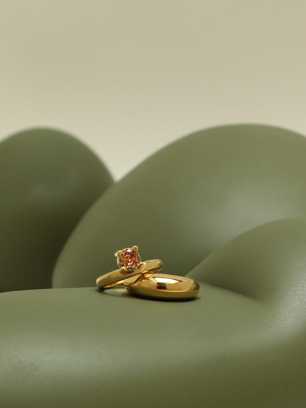 Drip ring with cubic zirconia showcasing an orange round stone in an oversized four-prong setting on a flowing green sculptural form.