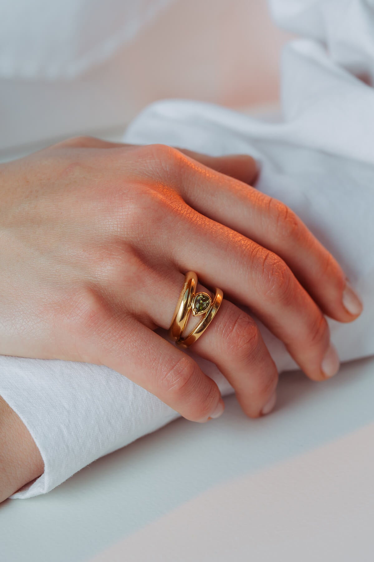 Drop ring with cubic zirconia showing contrasting rounded and angular bands framing a green drop-shaped cubic zirconia on hand.