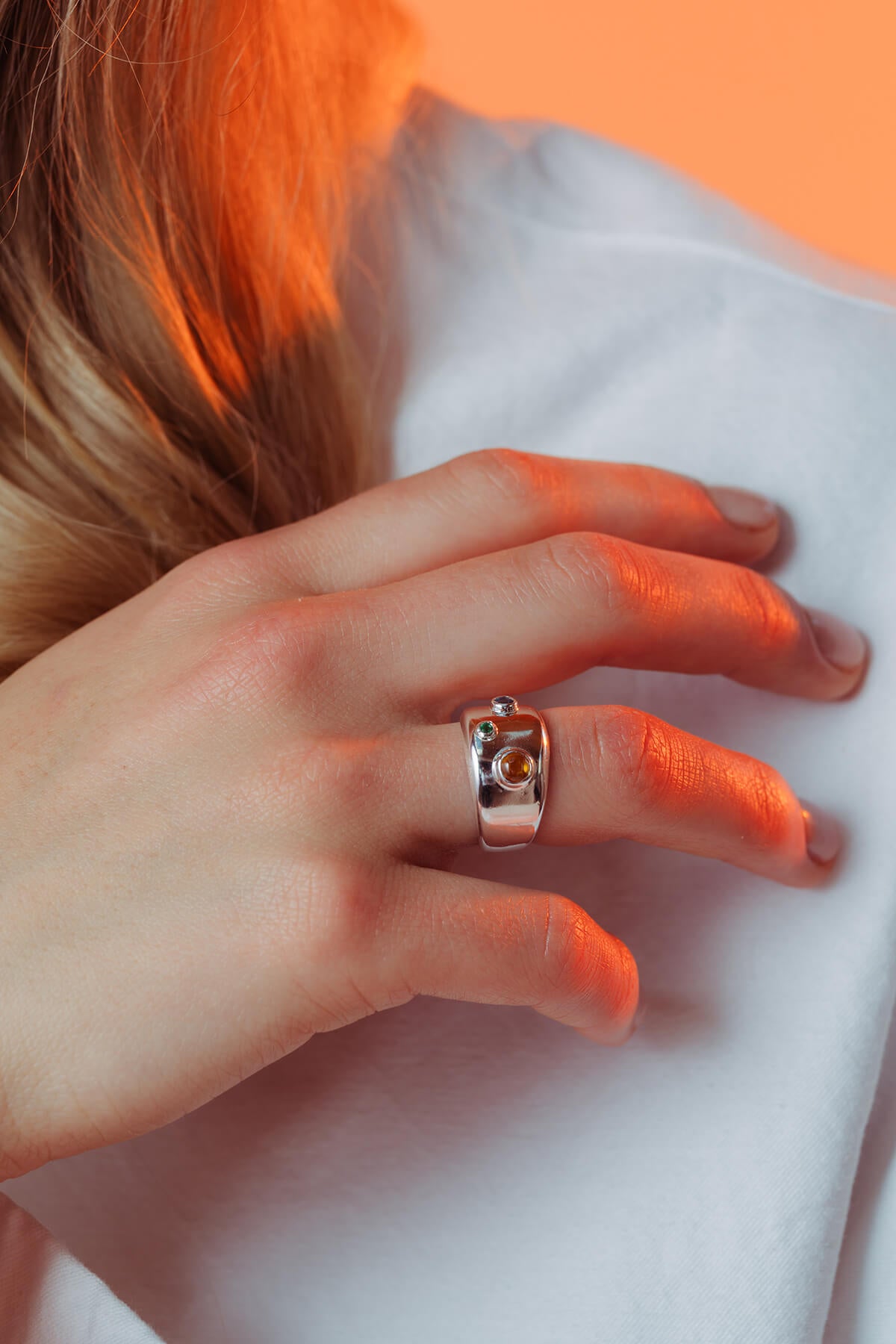 Spill ring with cubic zirconia shown on the finger with three colored cubic zirconia stones set across the polished band.
