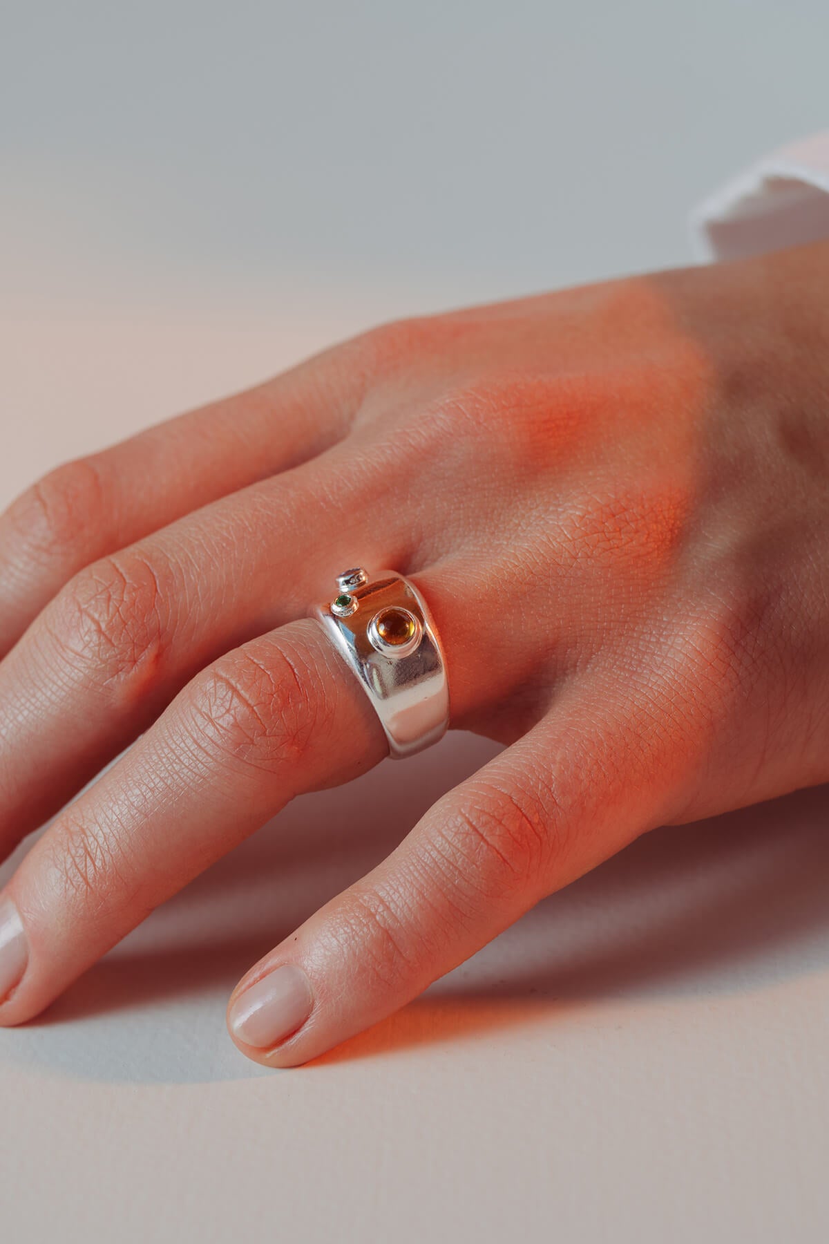 Spill ring with cubic zirconia worn on the hand showing three bezel-set blue, green and orange cubic zirconia stones.