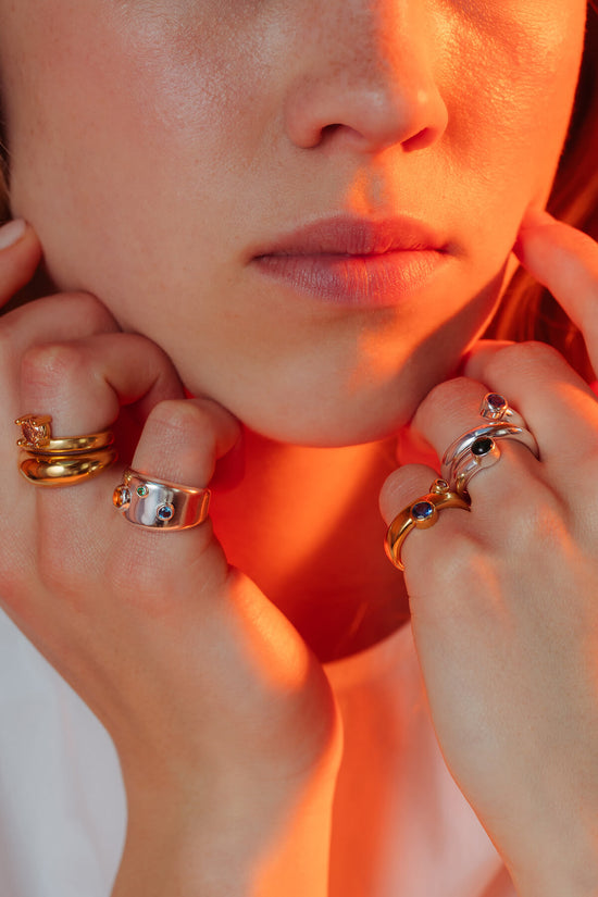 Drip drop rings styled on both hands with silver and gold rings featuring blue, green and orange cubic zirconia.