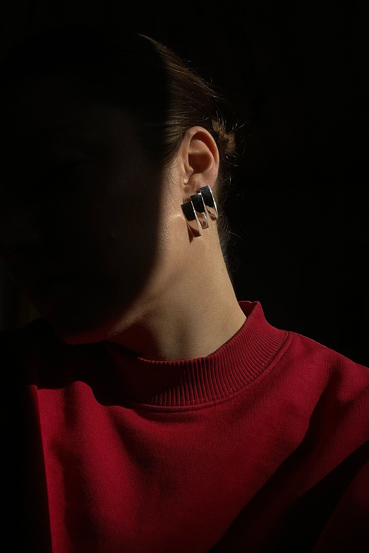Silver Studio Collect Pleat Earrings presented on Magaly wearing a red sweater in a dark setting. 