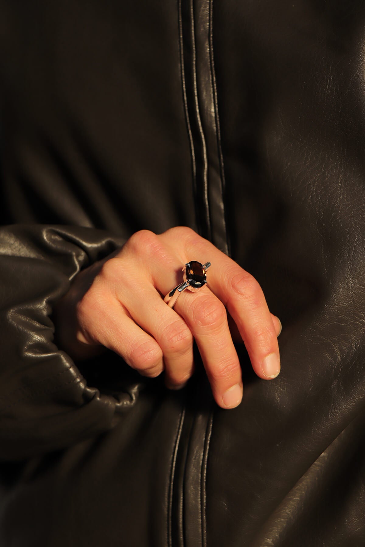 Lifestyle image of our Echo ring in sterling silver, worn on the hand, featuring a bold geometric band and an oval smoky quartz gemstone, styled with a dark leather jacket.