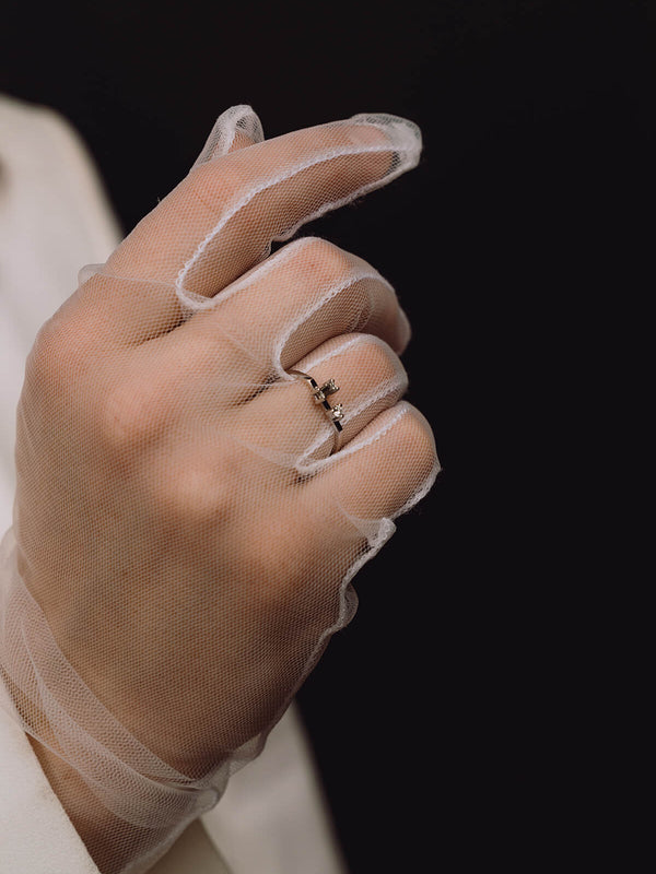Close-up of the Rune engagement ring in 18-carat white gold on a model’s ring finger, wearing a white lace glove. The ring features a flat-topped rounded square band, set with a brilliant-cut and a baguette-cut diamond.