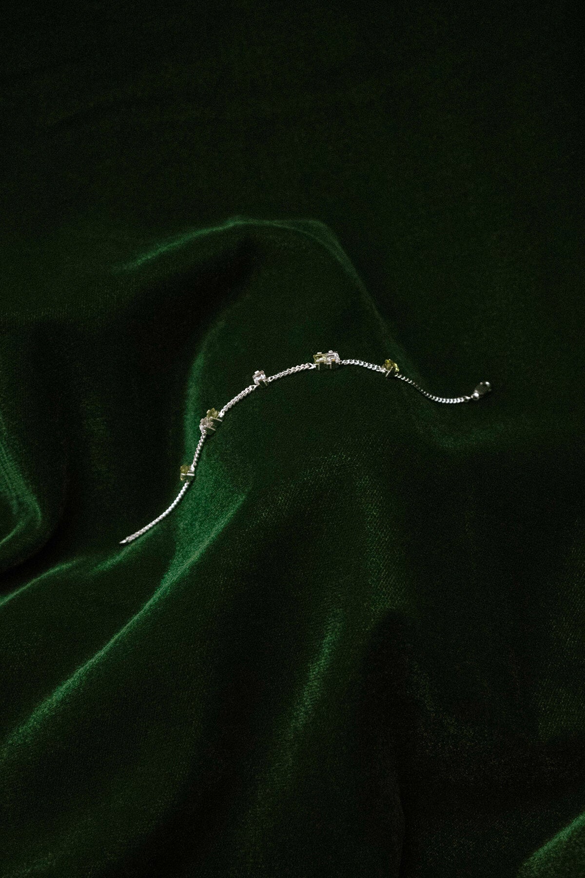 Image of a silver Eternal Bracelet with peridot and quartz crystal, luxuriously draped on a green velvet fabric.