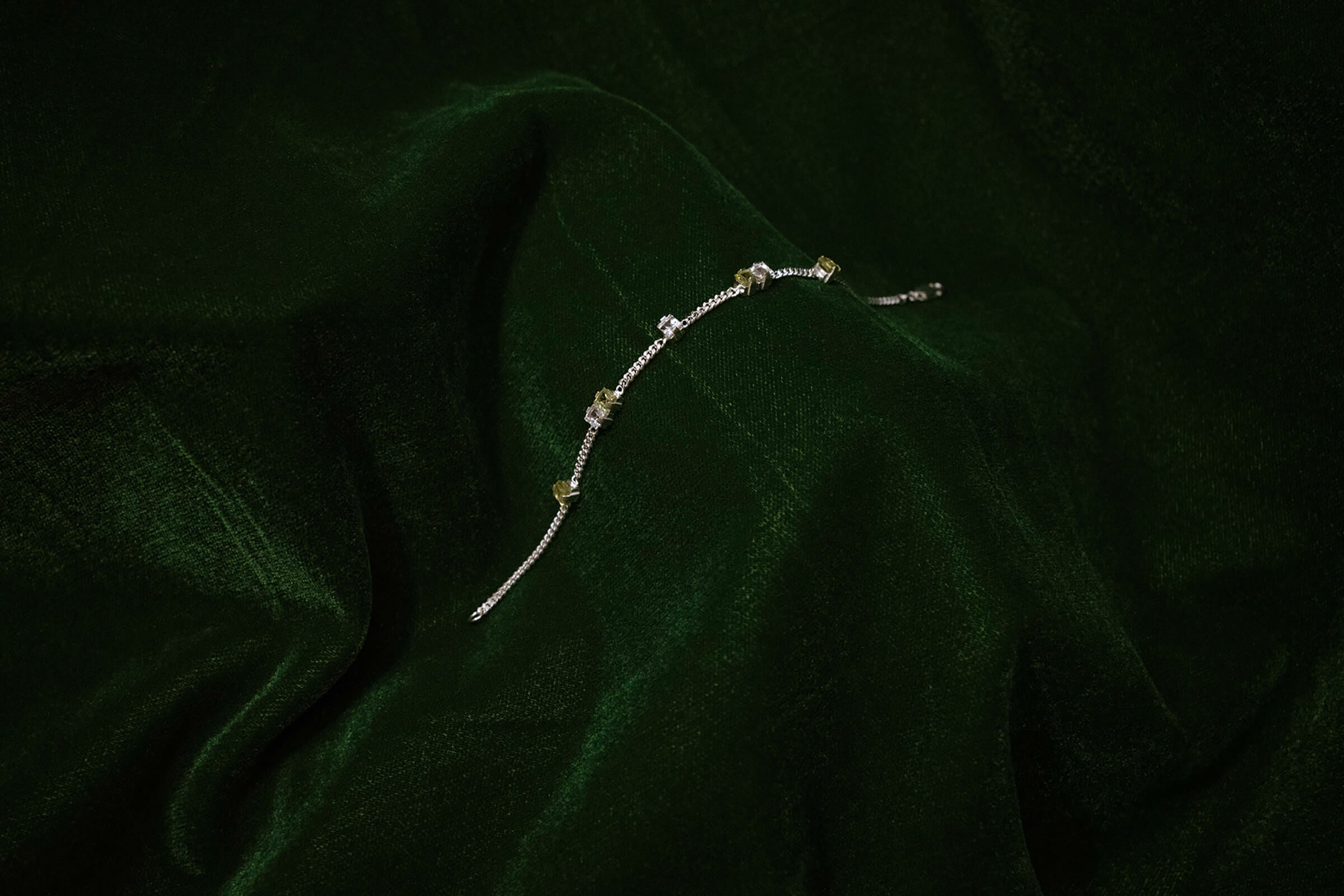 Silver Eternal Bracelet with peridot and quartz, resting on green velvet.
